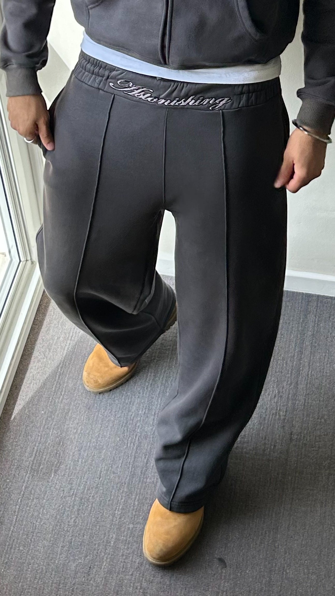 Person wearing dark gray jogger pants with a visible brand logo, standing indoors.